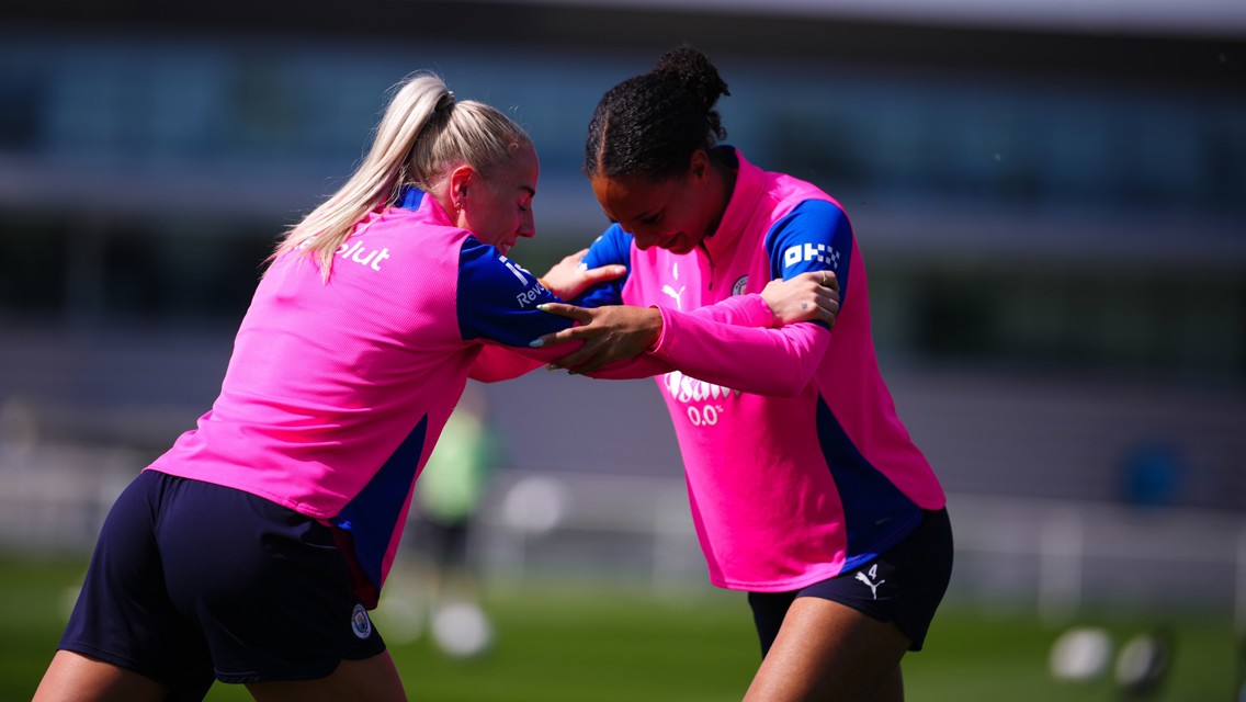 Two athletes in pink training kits practicing together on a field.