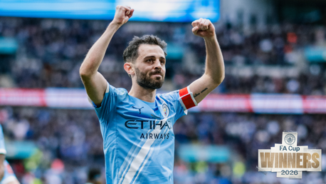 A Manchester City player with arms raised, wearing a blue jersey with sponsorship logo, celebrating at a stadium. The text 'FA Cup Winners 2026' appears on the image.
