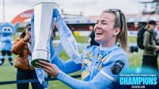 A person in Manchester City kit holds the Barclays Women's Super League trophy for the 2025/26 season. A mascot is visible in the background.