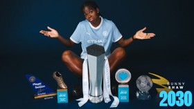 A football player in a Manchester City jersey surrounded by several trophies and awards, including a Golden Boot and Player of the Season.