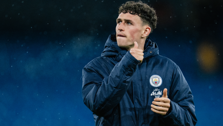 A person wearing a Manchester City warm-up jacket with club logos visible.