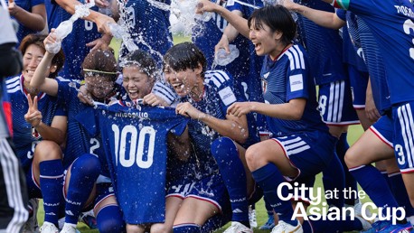 Japanese female soccer team celebrating at the Asian Cup. Players in blue jerseys with number 100, pouring water in celebration.