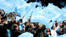 Fans holding blue flags that read 'Champions 2020/21' celebrating Manchester City's championship.