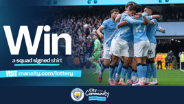 Promotional image for a contest to win a Manchester City squad signed shirt, featuring a group of players in blue uniforms celebrating together on the field. Includes a URL and logos for Manchester City and City in the Community.