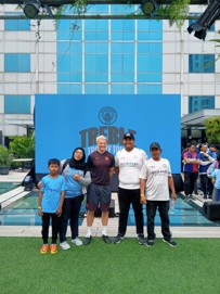 Group of people posing in front of a Manchester City Treble Trophy Tour backdrop inside a modern building with a pool.
