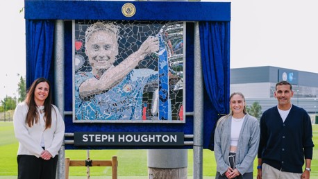 Three people are standing beside a mosaic depicting a football player with a trophy. The mosaic features the name 'Steph Houghton'.