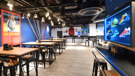 A sports-themed restaurant interior featuring tables and chairs, a Golden Boot display, sports jerseys on walls, and a colorful shoe showcase.