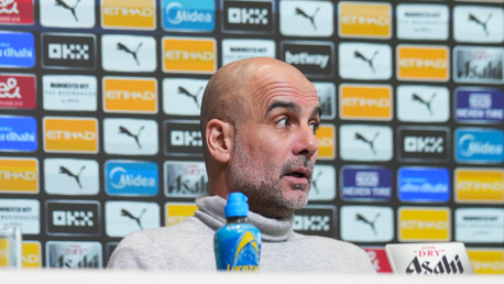 Person at a press conference with a backdrop featuring multiple sponsor logos including Etihad, Puma, and Asahi.