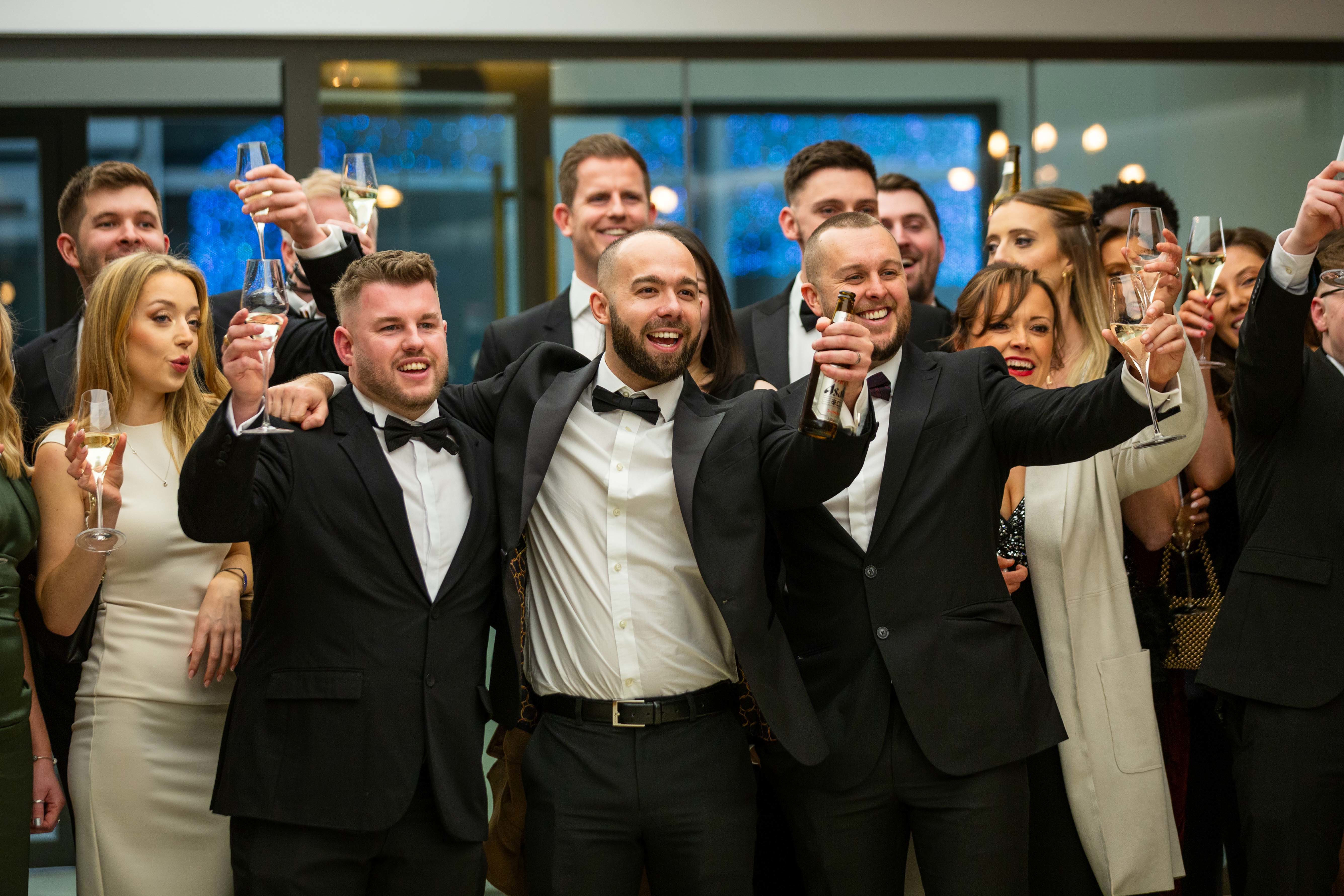 A group of people dressed in formal wear, making a toast with glasses at a celebratory event.