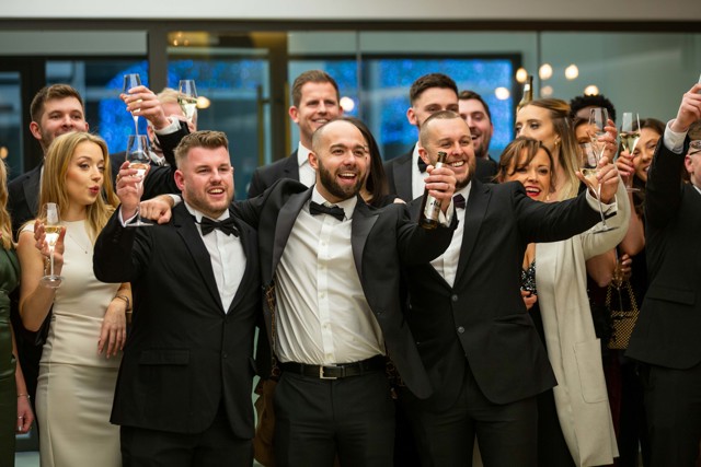 A group of people dressed in formal wear, making a toast with glasses at a celebratory event.