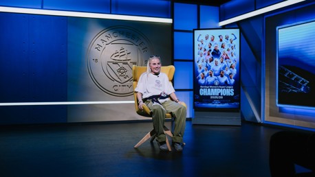 A person seated in a Manchester City studio with a backdrop featuring the club logo and a poster celebrating the Women's Super League champions for the 2025/26 season.