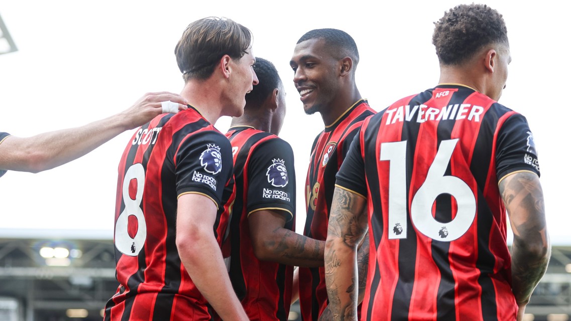 A group of AFC Bournemouth players wearing red and black jerseys, celebrating. Two jerseys have names 'Scott' and 'Tavernier' with numbers 8 and 16.