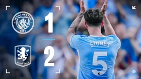 Scoreboard showing Manchester City 1-2 Aston Villa. A player with the name Stones on jersey clapping.
