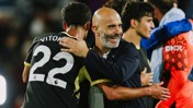 A bald man in a dark jacket hugging a soccer player wearing a black jersey with the number 22 and 'VITOR' on the back. Other people are in the background.