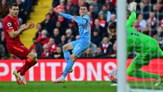 A soccer player in a light blue kit attempts a goal against a team in red. The goalkeeper is wearing a green kit.