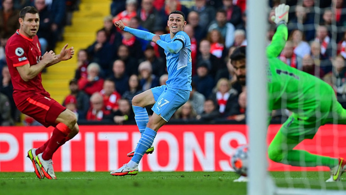 A soccer player in a light blue kit attempts a goal against a team in red. The goalkeeper is wearing a green kit.