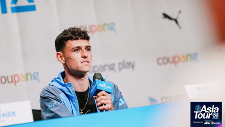 A person holding a microphone at a press conference for the Asia Tour '26. The background displays logos and text including 'Coupang' and 'Puma'.