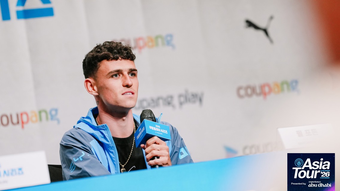 A person holding a microphone at a press conference for the Asia Tour '26. The background displays logos and text including 'Coupang' and 'Puma'.