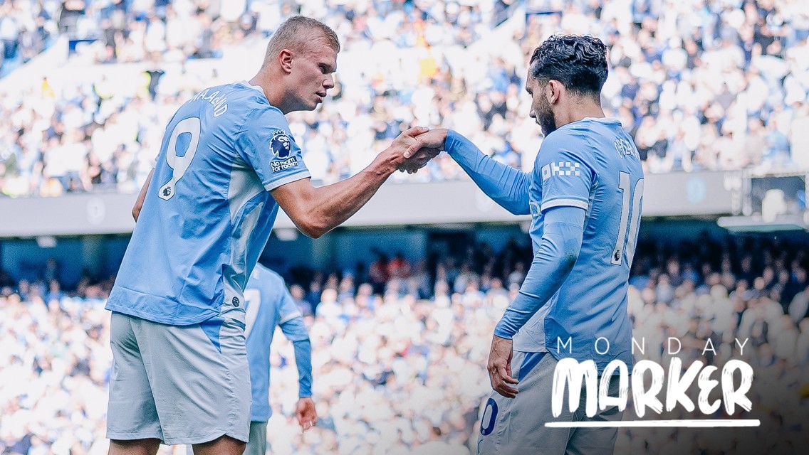 Two Manchester City players in blue jerseys are on the field performing a fist bump. The text 'Monday Marker' is visible in the bottom right corner.