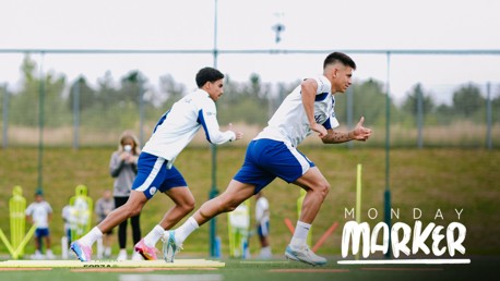 Football players sprinting during a training session. White text reads 'MONDAY MARKER' on the right side. Focused on speed drills.