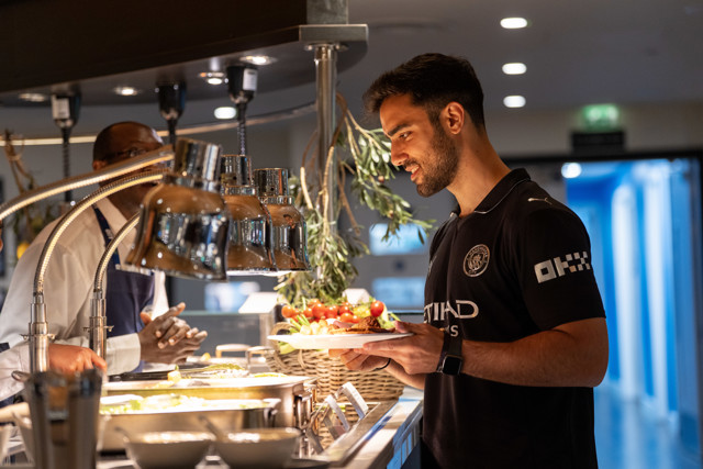A man in a Manchester City shirt selects food from a buffet.