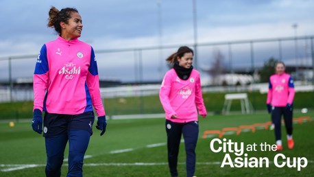 Three players from Manchester City Women's team in pink training kits on a field with the text 'City at the Asian Cup'.