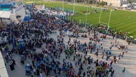 A large crowd gathered outside a stadium near a green field with people wearing various team colors and engaging in activities.