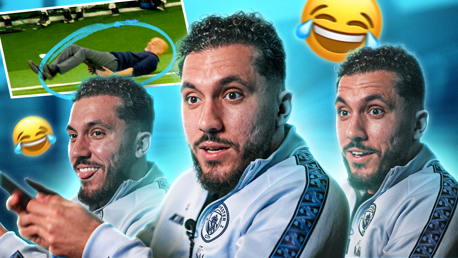 A football player appearing amused during an interview. The background includes a photo of an older man lying on the grass, surrounded by laughing emojis. The player is wearing a Manchester City jacket.