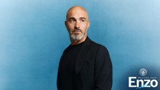 A man with a bald head and grey beard wearing a black jacket against a blue background. Text reads 'Welcome back Enzo' with a Manchester City logo.