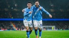 Two Manchester City players celebrating a goal on the field wearing the team kit at the Etihad Stadium.