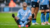 Manchester City player in light blue kit sitting in a meditation pose on the field during a match, with blurred face