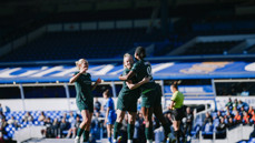 Football players in green jerseys celebrating on the field with a scoreboard in the background.