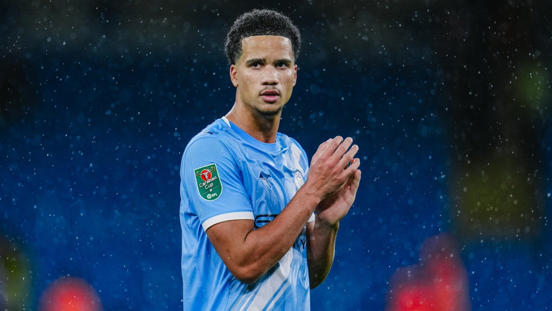 A football player in a light blue kit is clapping in the rain. The kit has a Carabao Cup patch on the sleeve.