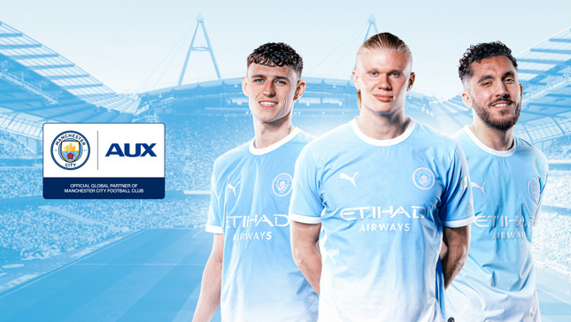 Three Manchester City players in the team's kit standing in front of a stadium background with Manchester City's and AUX's logos displayed.