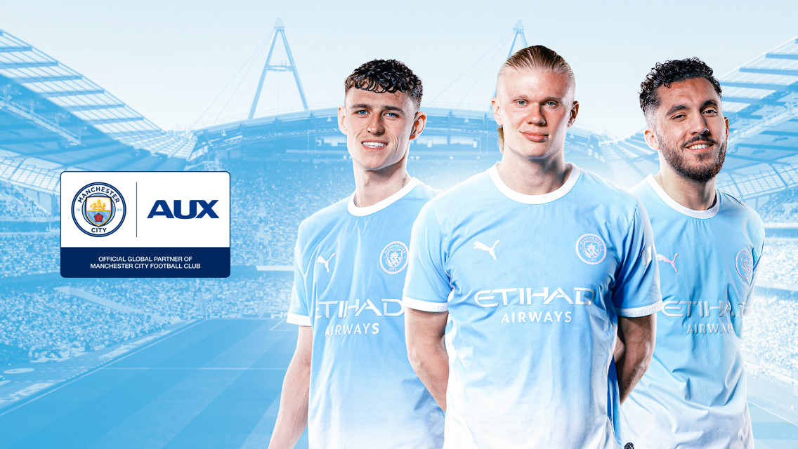 Three Manchester City players in the team's kit standing in front of a stadium background with Manchester City's and AUX's logos displayed.