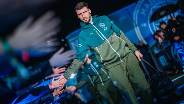 Manchester City player in olive tracksuit greeting fans outside Manchester City team bus.