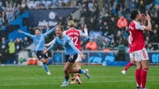 Football players in blue and red jerseys celebrate a goal in rainy weather on a crowded stadium field.