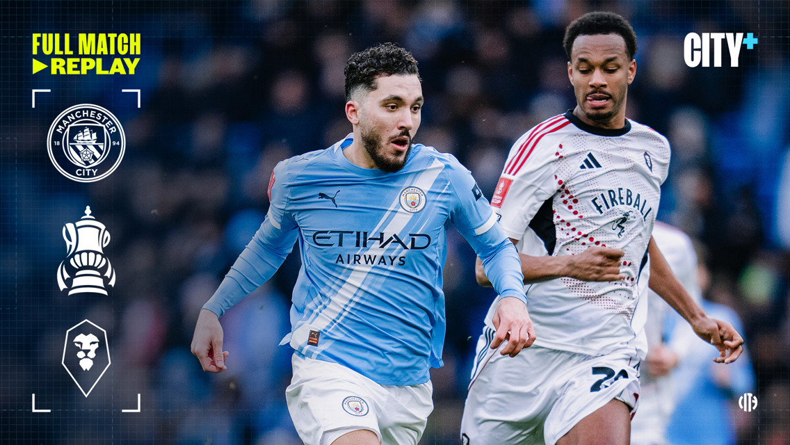 Manchester City player in a blue kit competes for the ball with a Salford City player in a white kit during an FA Cup match, as part of a full match replay on CITY+.