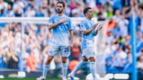 Two Manchester City players standing on the field wearing light blue kits with the number 20 visible on one player's shorts.