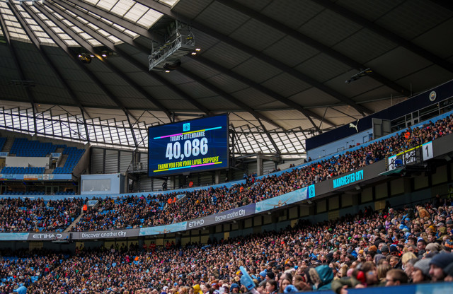 Image showing the attendance of a Manchester City match at the Etihad Stadium, with a large screen displaying 'Today's Attendance: 40,086 Thank You for Your Loyal Support.' The crowd is visible and the stadium interior is showcased.
