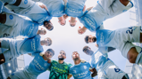 Manchester City players in a huddle wearing light blue jerseys with Etihad Airways sponsor visible, photographed from below looking upwards at a stadium setting.