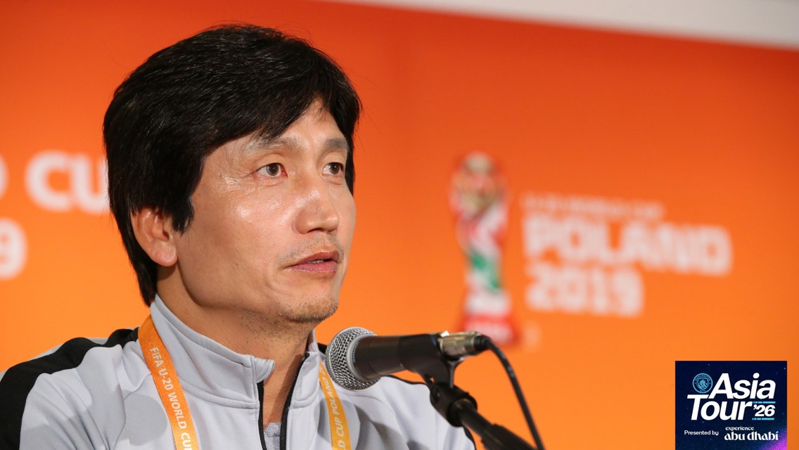 Individual speaking at a press conference for the 2019 FIFA U-20 World Cup. Background features event branding for the Asia Tour '26.