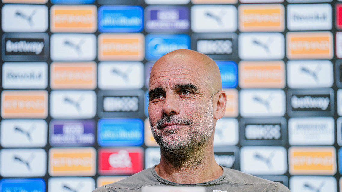 A person with a blurred face at a press conference with a backdrop filled with sponsor logos including Puma and Etihad.