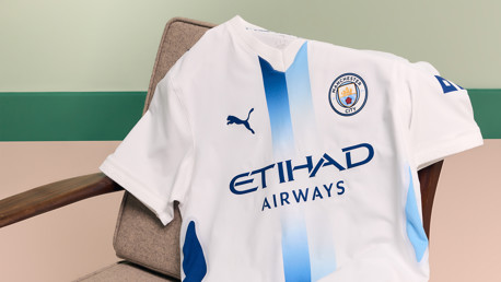 A white Manchester City football jersey with blue accents, featuring the Puma logo and Etihad Airways sponsor. The jersey displays the Manchester City crest.