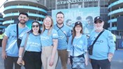 A group of people wearing Manchester City jerseys posing in front of the Etihad Stadium.