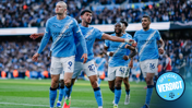 Manchester City players in blue jerseys celebrating on the field with a crowd in the background. An 'Official Verdict' badge is visible.