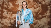 A person wearing a Manchester City jacket holding a Barclays trophy, with a medal around their neck.