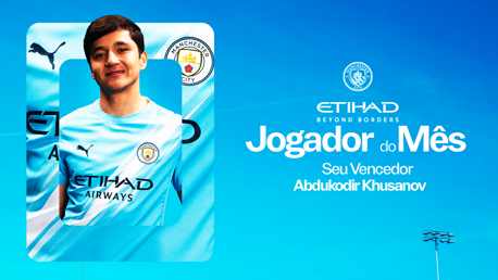 A Manchester City player is featured in a promotional image for 'Player of the Month' with the name Abdukodir Khusanov. The background is blue with Manchester City and Puma logos visible.