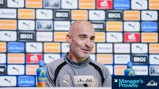 A man in a Manchester City jacket speaks at a press conference. The background displays various sponsor logos including Puma and Etihad.