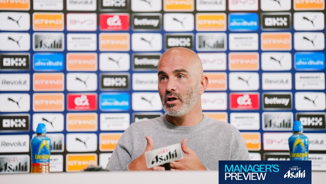 A person speaking at a press conference with a backdrop displaying various brand logos, including Puma and Asahi Super Dry. The sign on the table reads 'Manager's Preview.'